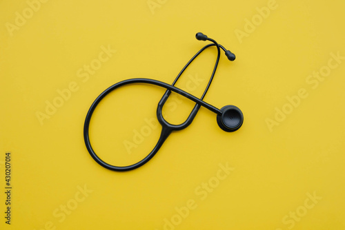 Black medical stethoscope on yellow background. Medicine and healthcare concept. Space for text. Flat-lay, top view.