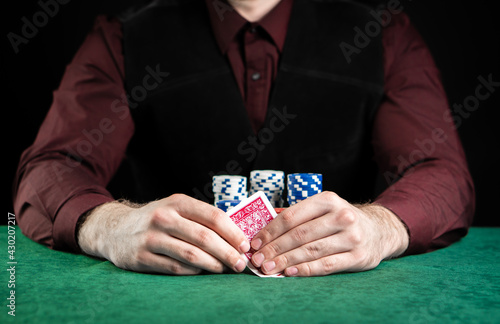 Young handsome poker player sitting at a green gaming table with a lot of chips and good cards.