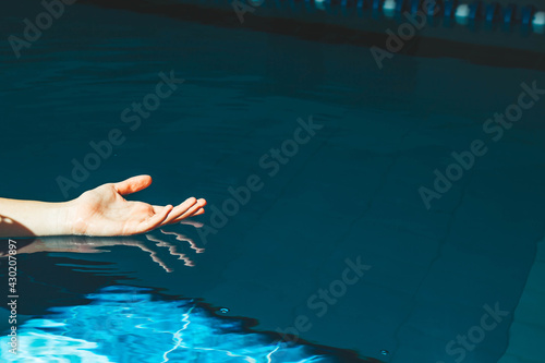 the swimmer's hand plunges into a water pool with blue transparent clear water, on which bright sunlight shines. indoor sports ground for swimming