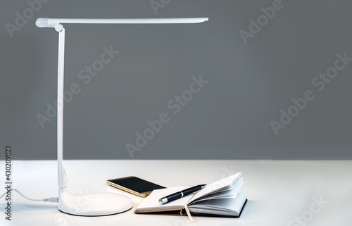 Photography A smartphone and open diary with a pen on the table under the desktop LED lamp
