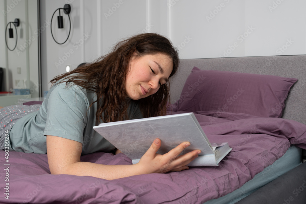 Happy woman lying on a bed. she watches photo album or reading a book. High quality photo Happy woman lying on a bed. she watches photo album or reading a book. High quality photo