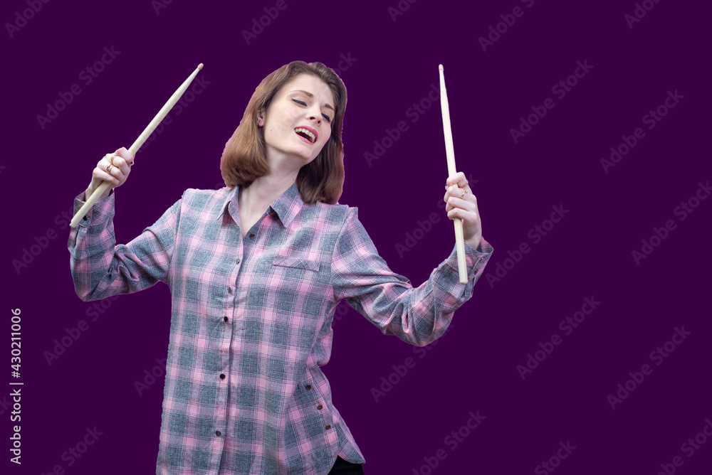 young beautiful girl, musician, holding drum sticks in hands. In a plaid shirt on a pink background young beautiful girl, musician, holding drum sticks in hands. In a plaid shirt on a pink background