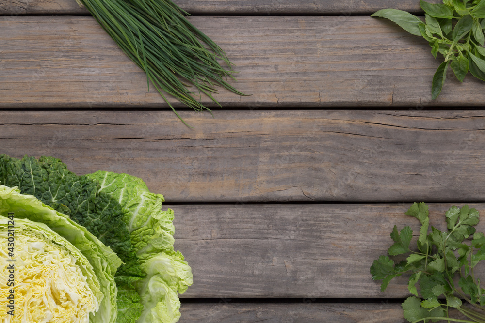 Fototapeta premium overhead view of rustic wood base with green cabbage, chives, basil and coriander