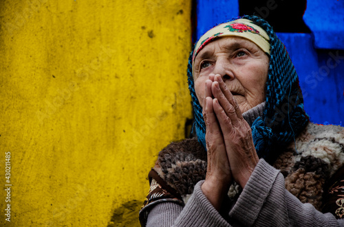 Grandmother prays on a yellow background close-up. An elderly woman in prayer. An old grandmother in a slum. Poor grandmother portrait photo. Poverty. Seniors concept.Old grandmother's prayer photo