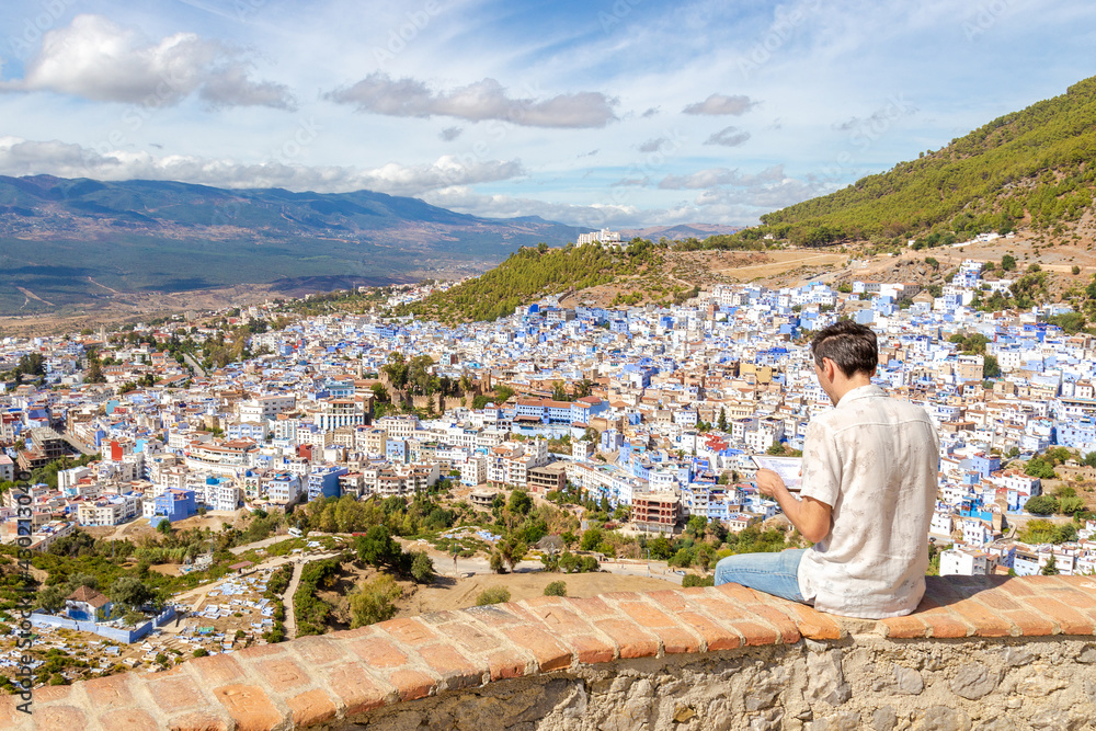 European man traveler creates a trip route and receives information about traveling using digital tablet of the town of Chefchaouen, Morocco.