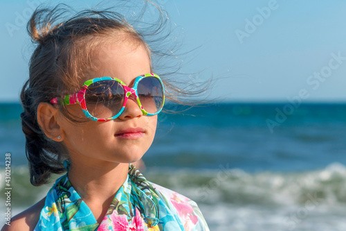 Little girl in a blue scarf on a background of the sea. Baby in sunglasses on a background of waves and sky