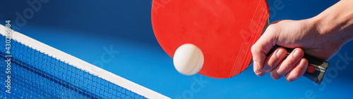 Hand with a ping pong racket hitting the ball above the table banner photo