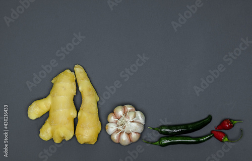 two roots of juicy fresh ginger, garlic head, sharp red and green peppers on a gray background, photographed close-up