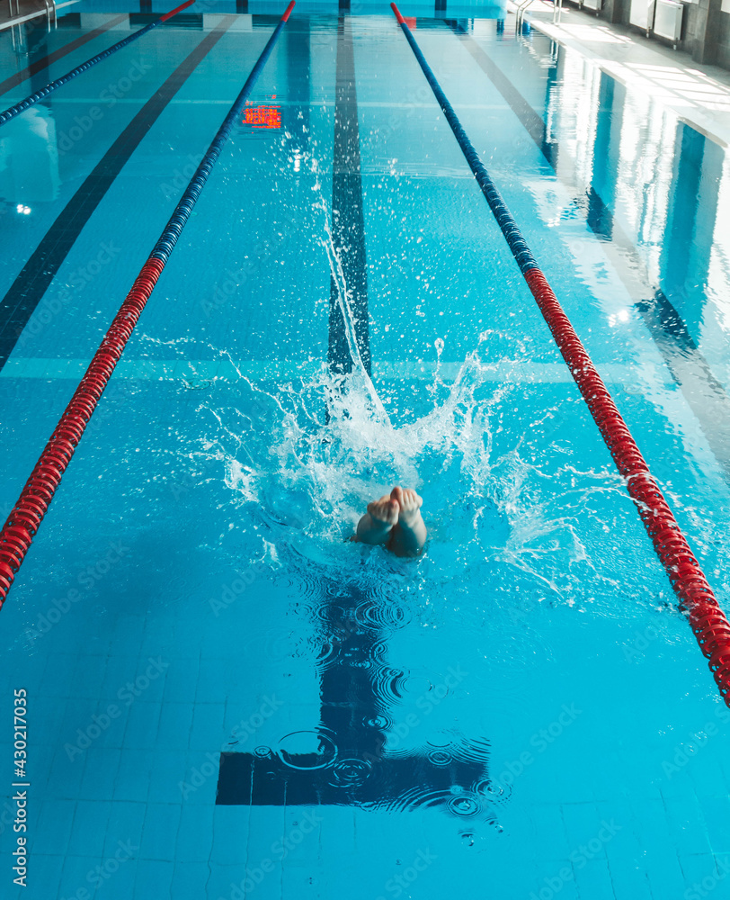 The swimmer pushes off the edge of the swimming pool. woman athlete jumps  into the water indoors. Stopping in motion. View from the back Stock Photo  | Adobe Stock