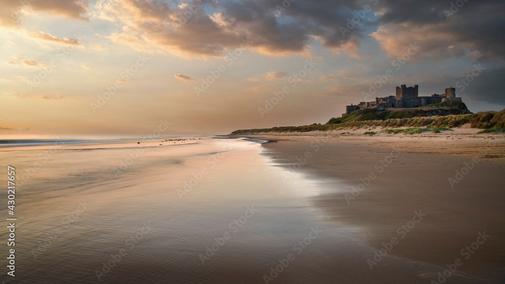 Beautiful majestic sunrise landscape of sunrise over beach with medieval castle ruins in background