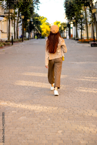 Fashionable girl walks around the city, the view from behind, the cap yellow, beige trousers, beige jacket, long hair. photo