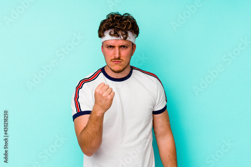 Young sport caucasian man isolated on blue background showing fist to camera, aggressive facial expression. © Asier