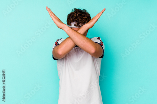 Young sport caucasian man isolated on blue background keeping two arms crossed, denial concept.