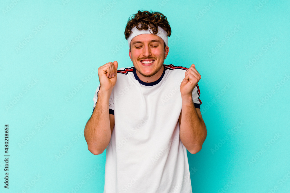 Young sport caucasian man isolated on blue background raising fist, feeling happy and successful. Victory concept. Young sport caucasian man isolated on blue background raising fist, feeling happy and successful. Victory concept.