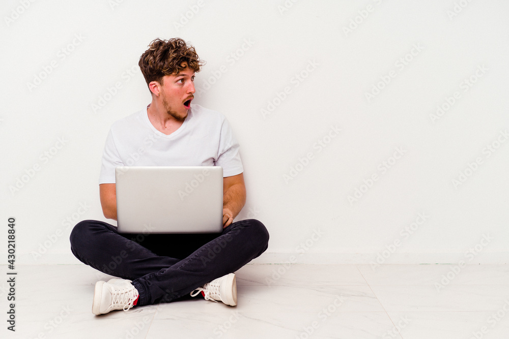 Young caucasian man sitting on the floor holding on laptop isolated on white background being shocked because of something she has seen. Young caucasian man sitting on the floor holding on laptop isolated on white background being shocked because of something she has seen.