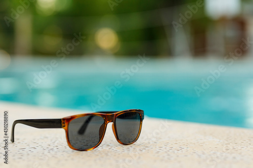 Summer holiday concept. Sun glasses near the swimming pool with crystal blue water.