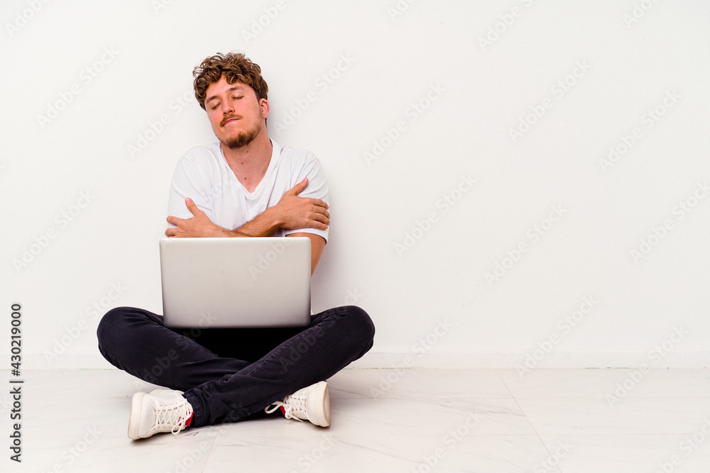 Young caucasian man sitting on the floor holding on laptop isolated on white background hugs, smiling carefree and happy. Young caucasian man sitting on the floor holding on laptop isolated on white background hugs, smiling carefree and happy.