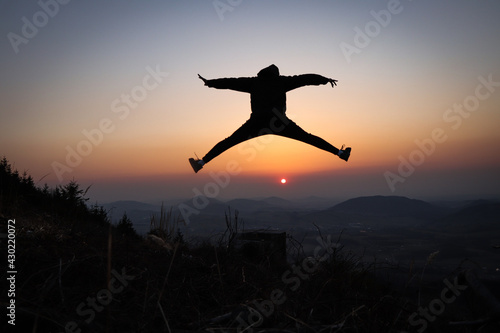 Photos Silhouette of a teenager and athlete jumping on a tree stump and doing a straddle vault, splits at sunset in the European mountains