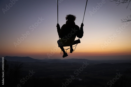 Hairy young boy aged 16-20 of European descent enjoys his life swinging on a swing at sunset on the top of Prasiva mountain in the Beskydy mountains in eastern Bohemia in Central Europe