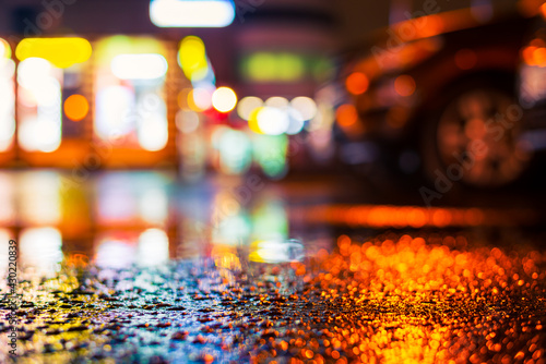 Rainy night in the city. Parking mall with cars. Reflections of shop windows on wet asphalt. Colorful colors. Close up view from the asphalt level.