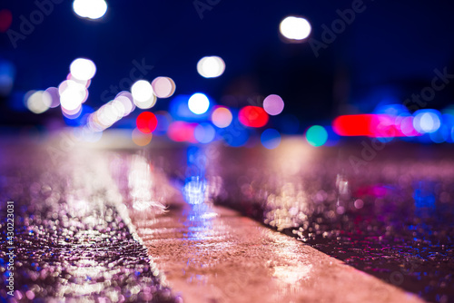 Rainy night in the city. Headlights driving cars. Reflections of street lamps on the wet asphalt. Colorful colors. Close up view from the level of the dividing line.
