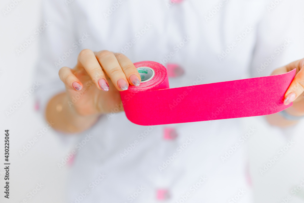 a roll with a pink tape in the hands of a nurse on a white background. a patch for the muscles. Sports event. a roll with a pink tape in the hands of a nurse on a white background. a patch for the muscles. Sports event.