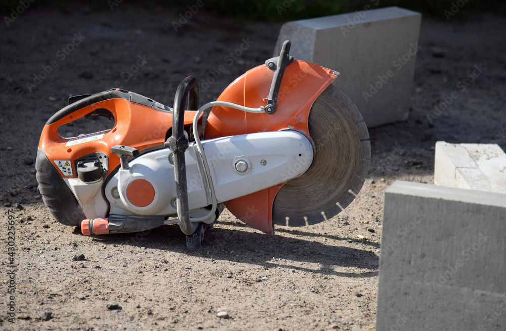 A circular saw lies on the ground between concrete curbs, a construction site.