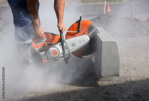 A worker saws a large concrete curb with a circular saw, road construction.