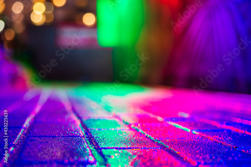 Rainy night in the city. Reflections of shop windows on the wet pavement. Colorful colors. Close up view from the pavement level.
