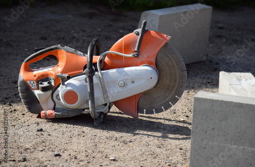 A circular saw lies on the ground between concrete curbs, a construction site.