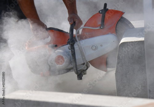 A construction worker saws a large concrete block with a circular saw,close-up.