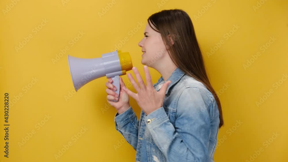 Side profile view sad young protesting woman scream in megaphone, angry caucasian girl does not hold back emotions, to shout furiously, wears denim jacket, isolated on yellow color wall background Side profile view sad young protesting woman scream in megaphone, angry caucasian girl does not hold back emotions, to shout furiously, wears denim jacket, isolated on yellow color wall background