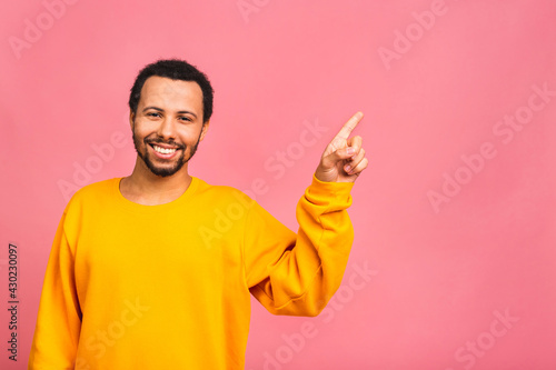 Portrait of a smiling happy african american black man in casual pointing with fingers aside isolated over pink background.