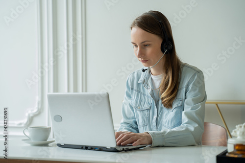 Female talking in a video conference on line with a headset with microphone and using laptop in office, consulting client