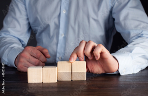 Wooden cubes on the table. Male businessman with hand puts the cube in a row.