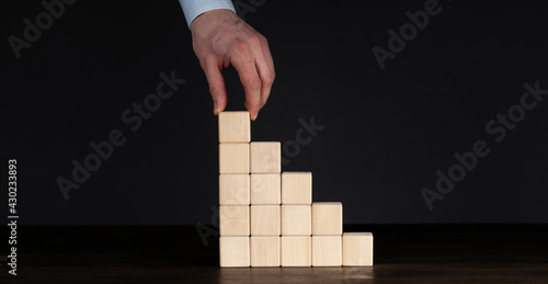 Wooden cubes on the table. The hand places the top cube on the top of the pyramid. Growth and profit concept. Business