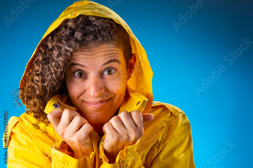 Mujer joven cabello enrulado sonríe con impermeable amarillo sobre fondo azul