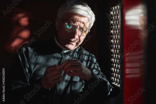 Tableau sur toile Senior priest sitting with rosary beads sitting in confessional and listening to