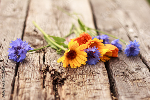 Beautiful blue cornflowers and calendula lay on rough wooden board. Bright summer bouquet. Summer background