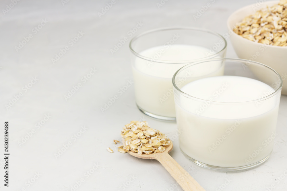 Dairy free oat milk in glasses and flakes on light background Dairy free oat milk in glasses and flakes on light background