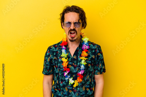 Young caucasian man wearing a hawaiian necklace isolated on yellow background screaming very angry and aggressive.