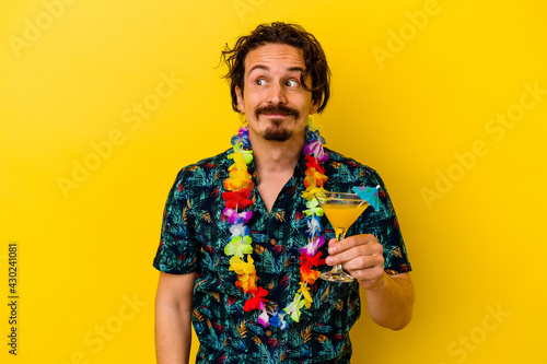 Young caucasian man wearing a hawaiian necklace holding a cocktail isolated on yellow background dreaming of achieving goals and purposes