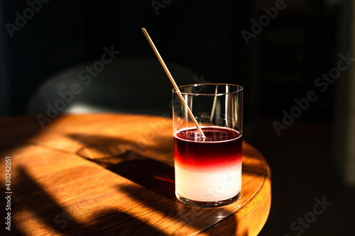 A sweet and sour refreshing blackberry gin bramble cocktail in a highball glass without ice in direct hard sunlight with long shadows, on a wooden table, horizontal photo with copy space photo