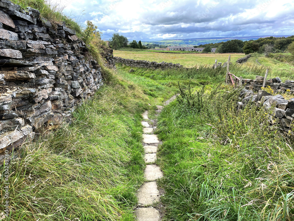 Country paved path, leading past a dry stone wall to, Allerton Quarry, Bradford, UK