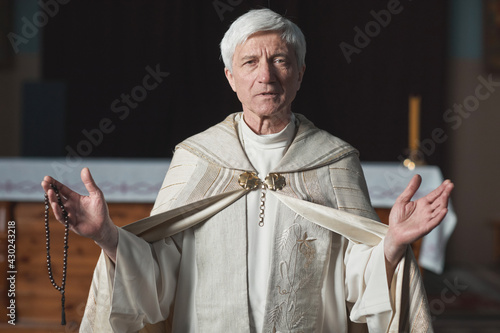 Fototapeta Portrait of senior priest in formal costume looking at camera and holding weddin