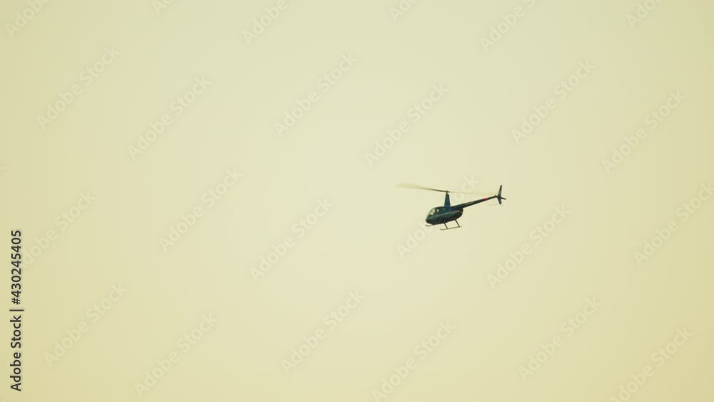 Aerial view of a helicopter flying against the clear white sky in the background during the daytime. High-quality video. The movement of Helicopter rotors can be seen. Aerial view of a helicopter flying against the clear white sky in the background during the daytime. High-quality video. The movement of Helicopter rotors can be seen.