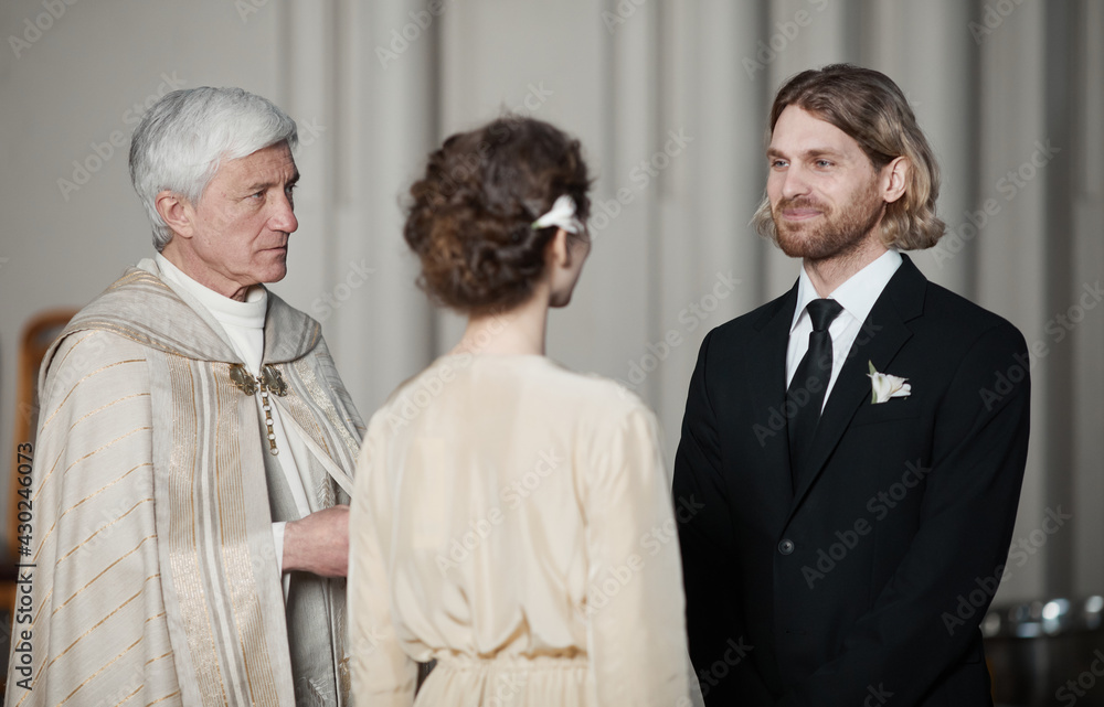 Young couple standing opposite each other and giving prayers at wedding ceremony with priest Young couple standing opposite each other and giving prayers at wedding ceremony with priest