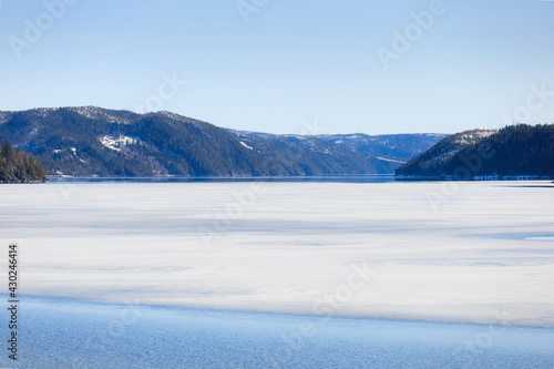 Lake thaw of Spring landscape. Forest lake partially covered with ice and partially reflected the blue sky and mountains, at the beginning of a spring day. © K-I foto