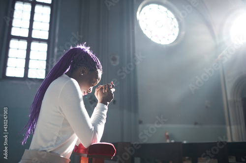 African young woman sitting in front of the altar in the church and praying photo