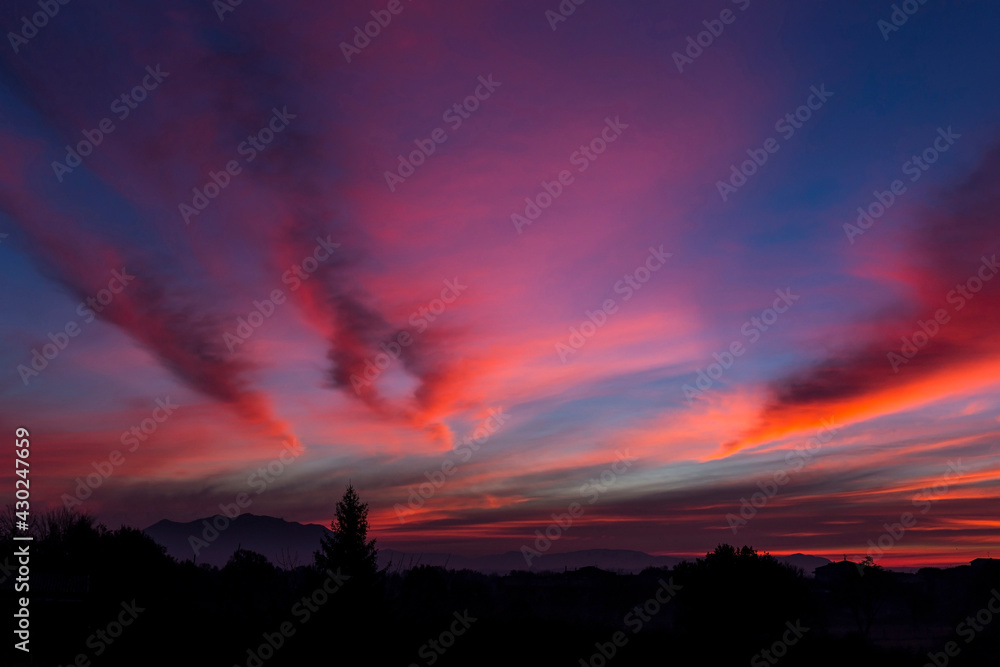 The intense colors of the dawn. The colored clouds cross the sky like flaming lines above the dark outline of Mount Soratte, in the Roman countryside.